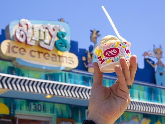 A hand holds a cup of Amy's Ice Cream, with the shop's sign in the background.