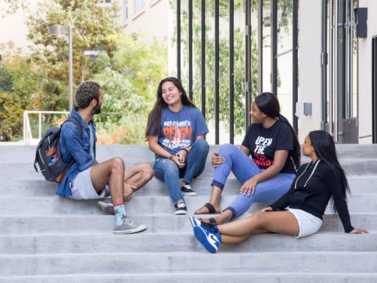 Four students sit on steps outside of St. Andre Apartments, hanging out and talking.