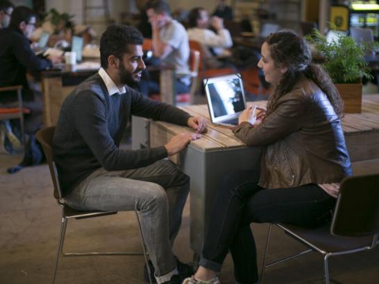 Two students sit across from one another and talk during a networking event at a coffee shop.