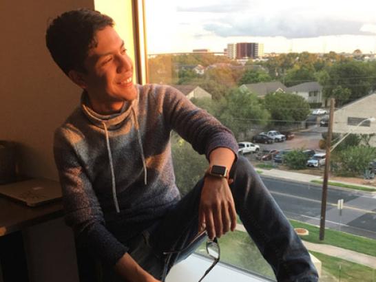 A student sits by a window, looking out and smiling