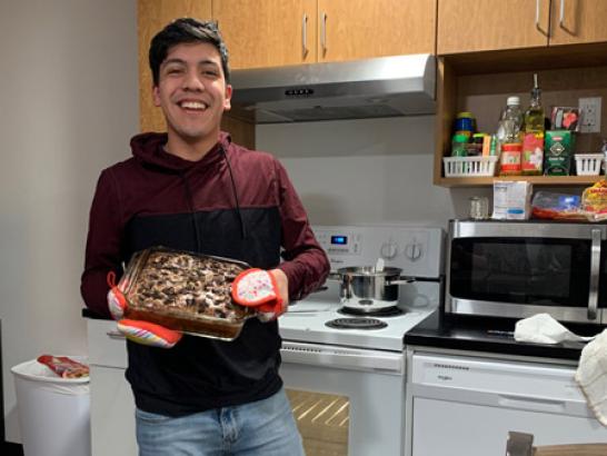 A proud looking student holding a meal he just made in a dorm kitchen