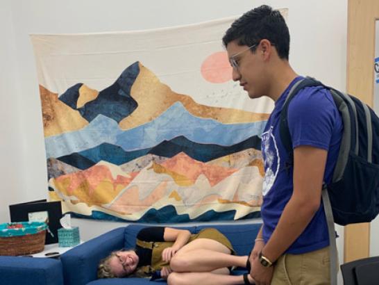 Two students in a dorm, one of them lying on the couch and the other standing