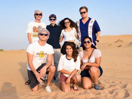 A group of seven students wearing casual clothing and sunglasses gather together for a group photo in a desert landscape while studying abroad in Dubai.