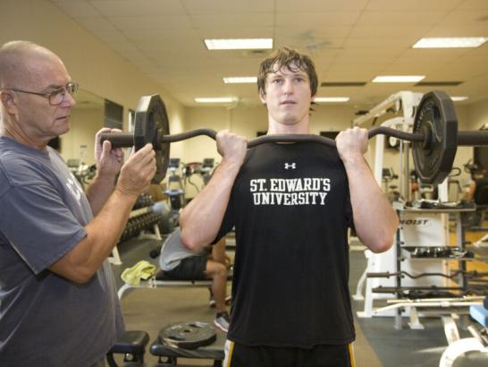 Kinesiology instructor guides a student through a weigh-lifting exercise