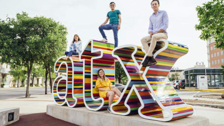 Four students sit and stand on a colorful 3D ATX sign.