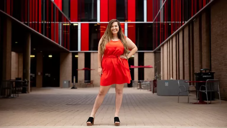 Jessica Riley wears a red dress and stands on the Village patio.