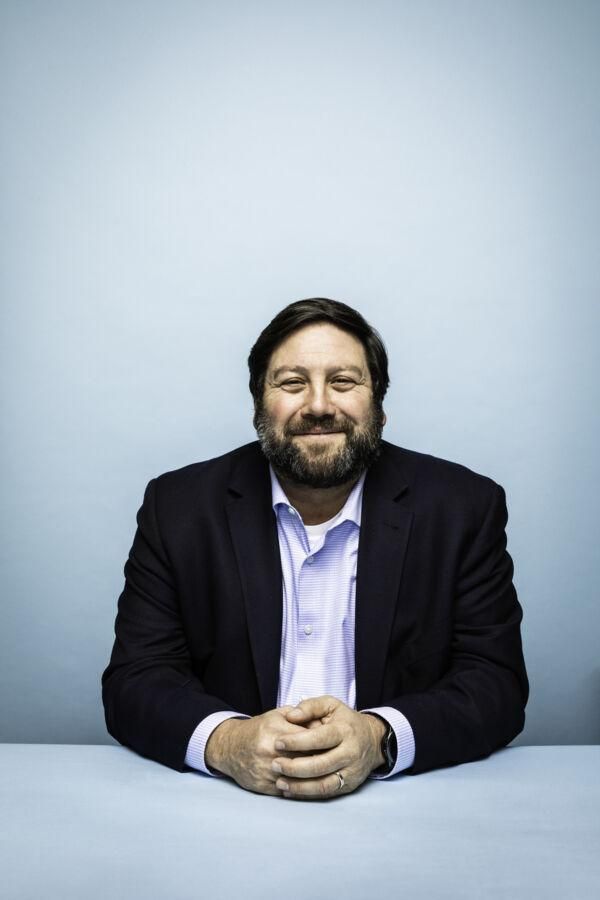 A portrait of David Altounian sitting in front of a light blue backdrop.