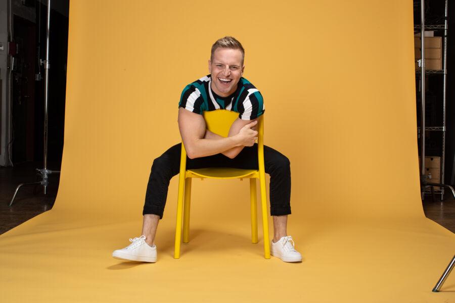 Tyler Mount sits on a yellow chair on a yellow backdrop.