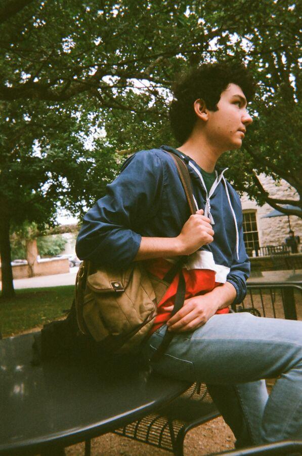 A student sits on a patio table with their backpack.