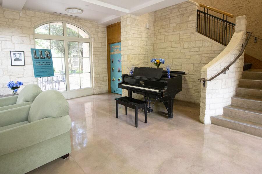 Two cushy green chairs next to a piano sitting by the window near the bottom of a winding staircase