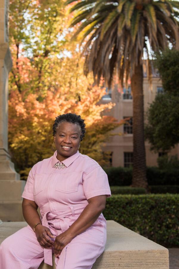 Mona Hick sits in a pink jumpsuit on Stanford's campus.