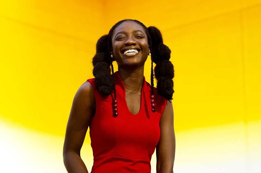 Kadija Samura smiles and stands in front of a warm gradient mural.