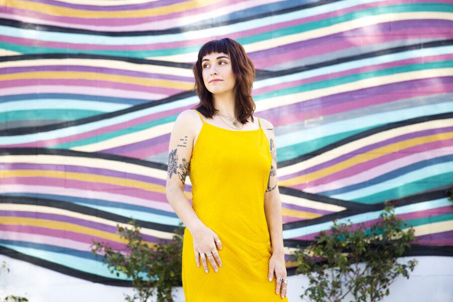 Maya Boehm wears yellow and stands in front of a colorful wavy mural.