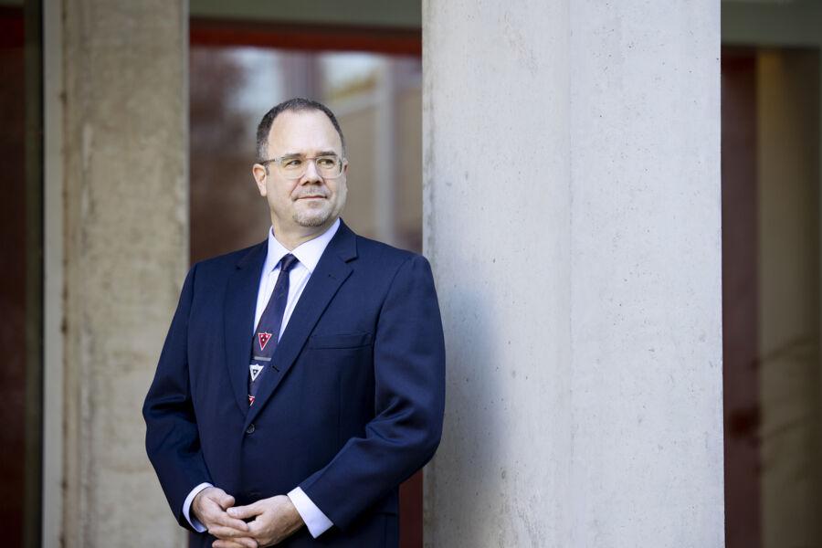 A man in a suit and glasses poses in front of a building