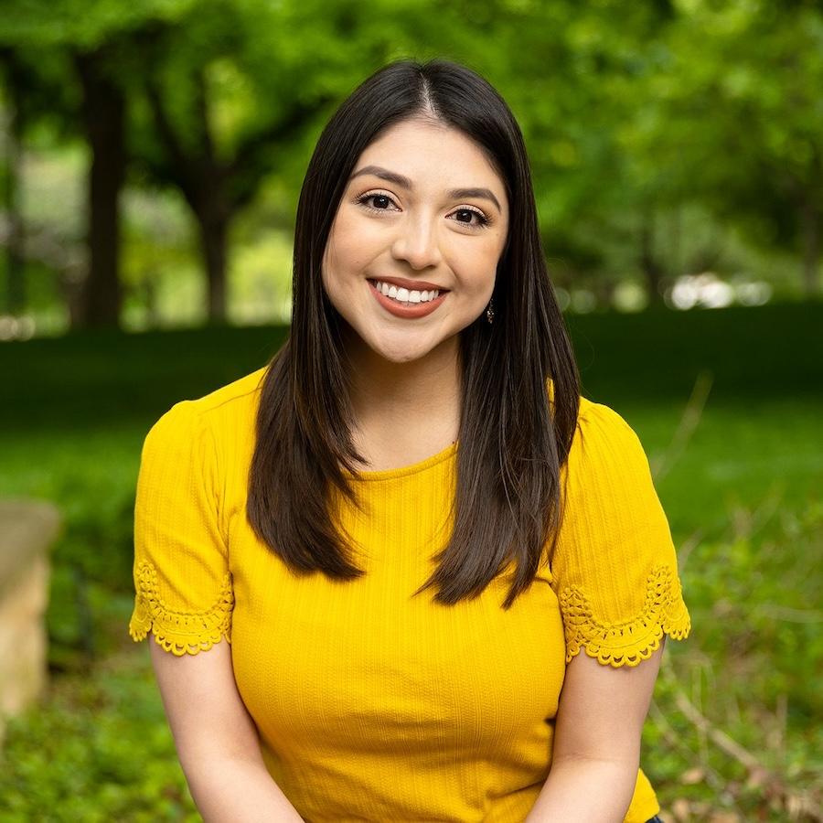 Victoria Garcia wears a yellow shirt and sits on Ragsdale patio. Greenery and trees are in the background.