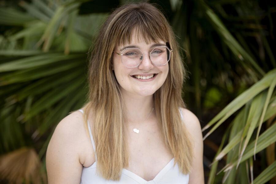 A woman with glasses sitting in front of palms smiling at the camer