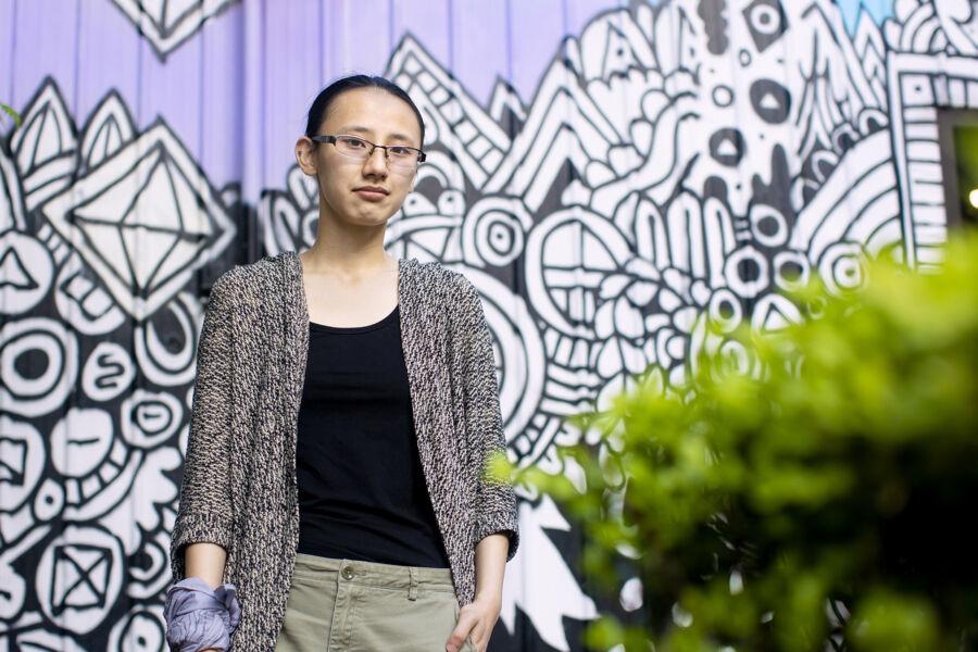 Murphy Chen stands in front of a black, white and purple mural in downtown Austin.