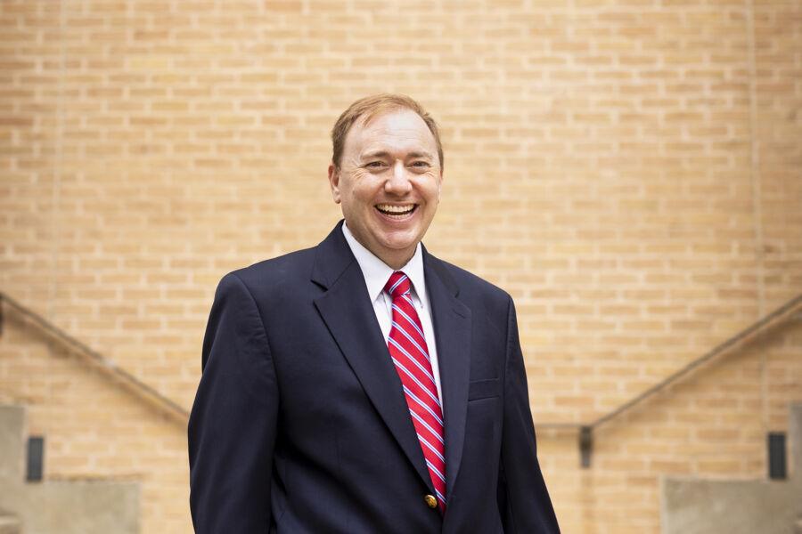 A man in a suit smiles in front of a brick wall