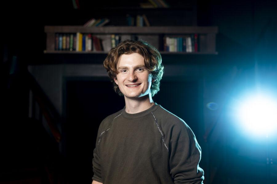 Andrew Mueller stands in the Mary Moody Northern Theatre with a set piece for a play behind him.