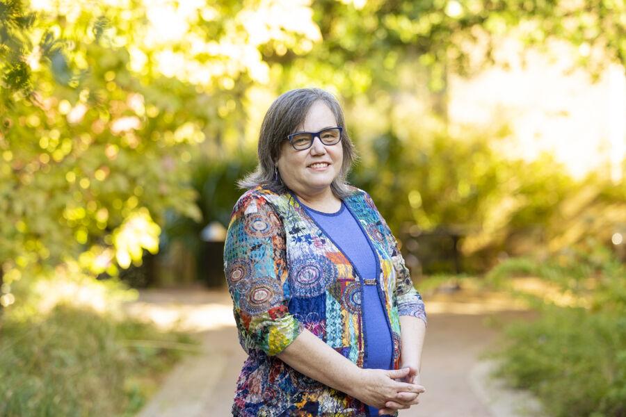 A woman smiles at the camera under a lush green tree