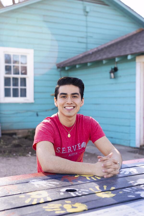 St. Edward's student Cristobal Diaz sits at a picnic table painted with colorful handprints.