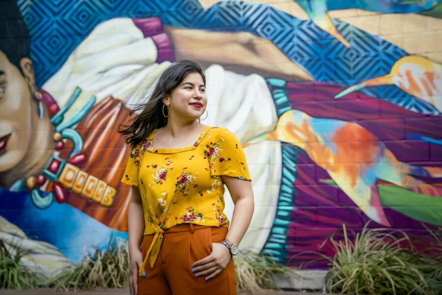 Bianca Esquivel stands in front of a mural depicting a larger-than-life Frida Kahlo.