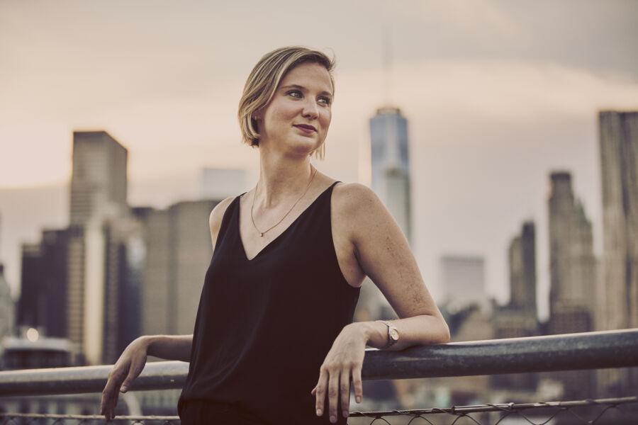 Lindsay Vick leans on railing with a skyline view of New York City behind her.