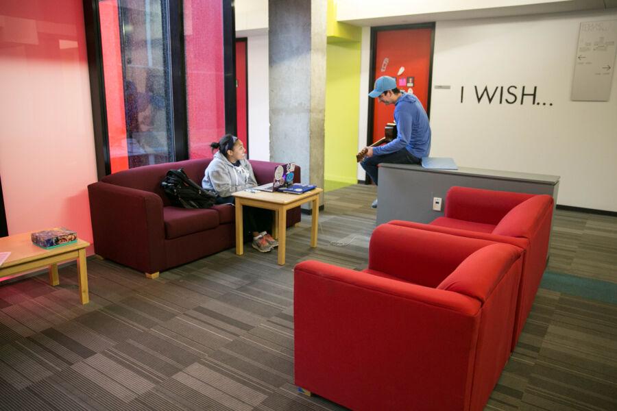 Two students talking in a brightly colored room, on red couches and chairs