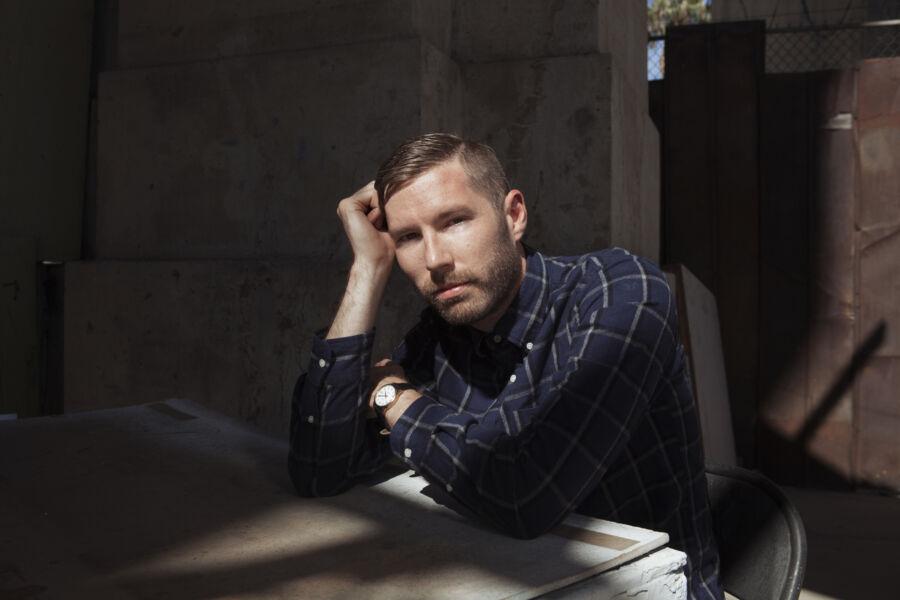 Charles Rogers leans on a table for a portrait in a shadowy room.