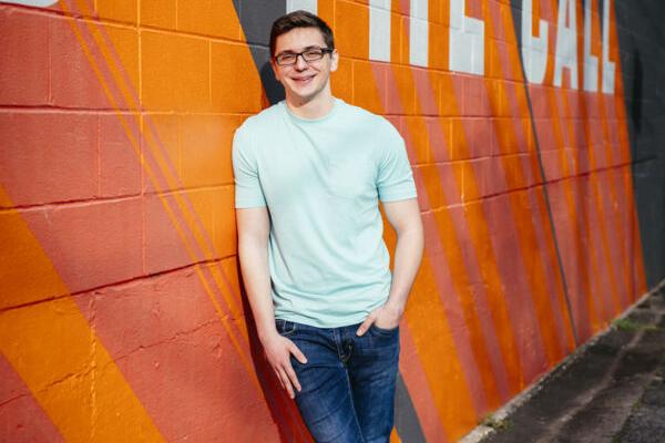 Josh Leikam leans on an orange wall.