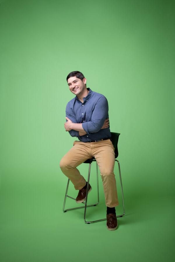 Leon Benegas sits on a barstool in front of a green background.