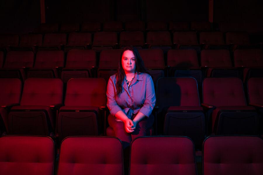 Kit Taylors is illuminated by red and blue lights as she sits in the seats of the Mary Moody Northen Theatre.