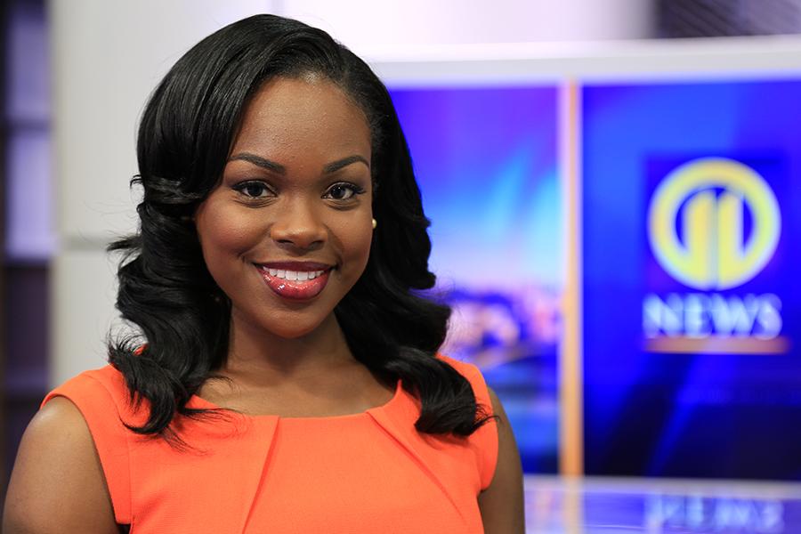 Marlisa Goldsmith stands in the newsroom with her news station logo on display.