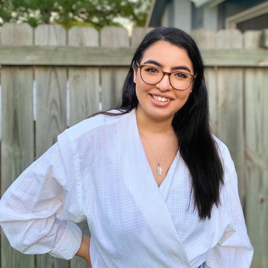 Rania Lewis wears a white blouse and glasses. A fence is in the background.