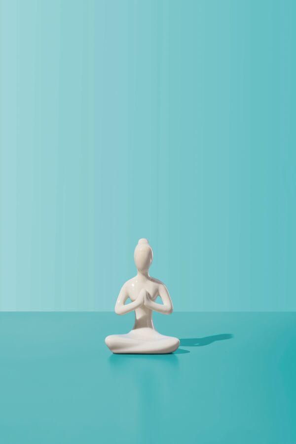 A white yoga figurine on a blue-green background.