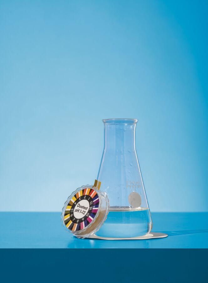 A water test kit leans on glass beaker on a blue background.