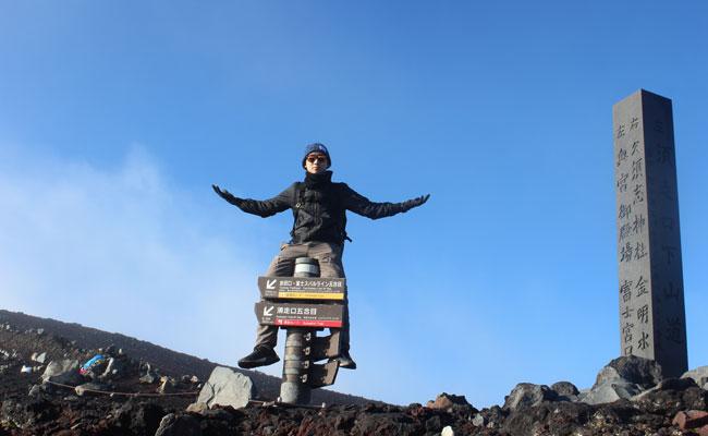 Brian To sits on a trail sign during a hike in Japan.