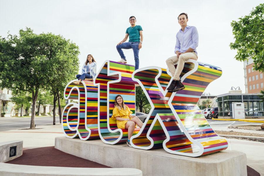 4 students sitting on a rainbow "atx" sculpture