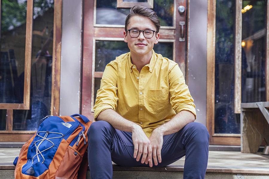 Cody Dzurisin sits with a backpack on a patio.