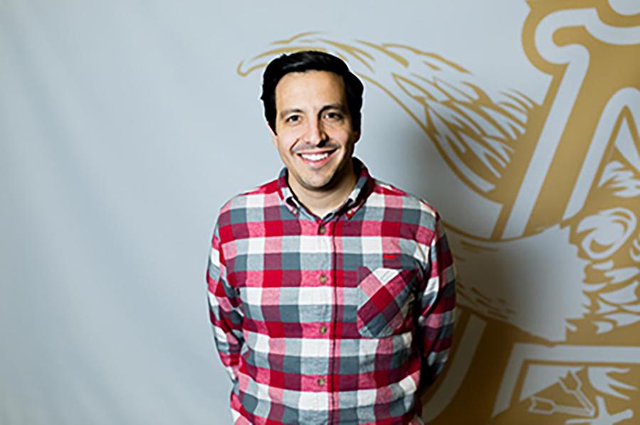 Jorge Almeida wears a black, white and red checkered shirt on a white and yellow backdrop.