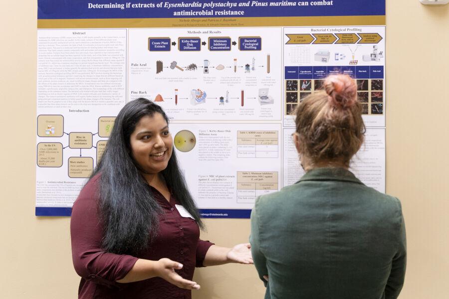 Science student at St. Edward's presents her science research poster to a fellow student to a